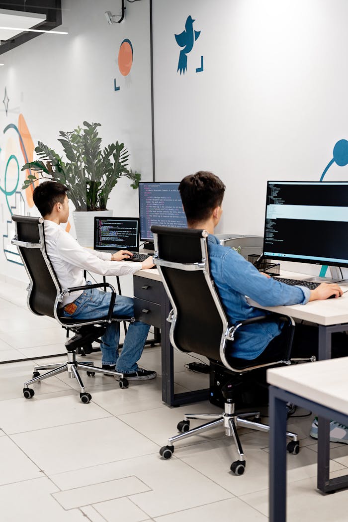 discover Two programmers collaborating in a bright, modern office, coding on monitors.